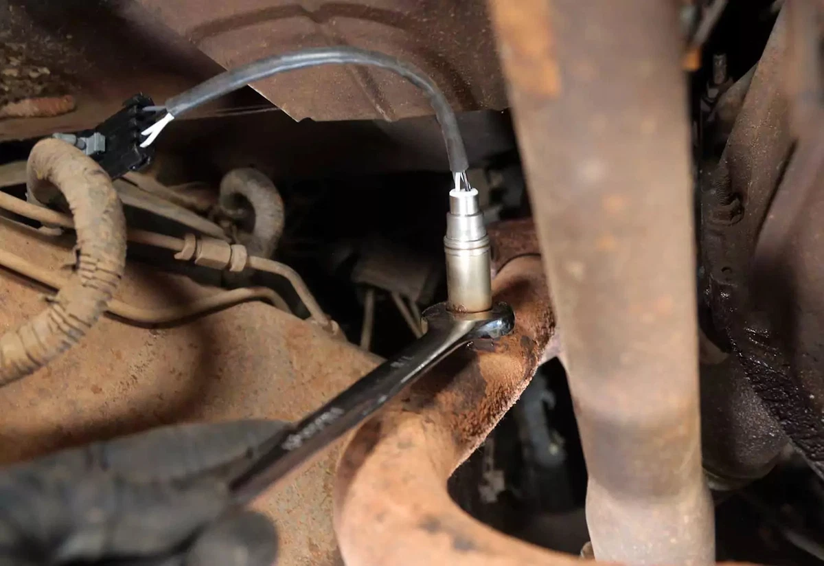 A mechanic tightens the new oxygen sensor in its bung with an open-end wrench.