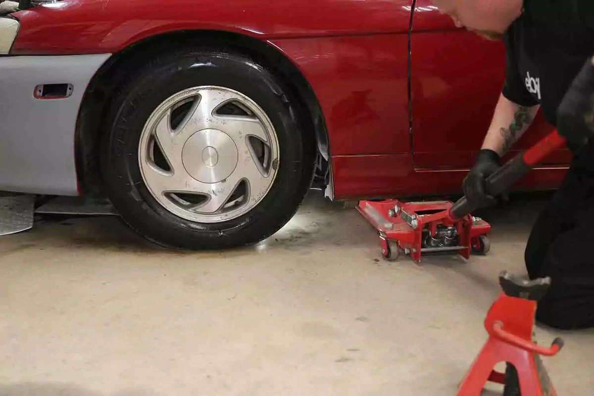 A mechanic rolls a floor jack under a vehicle.