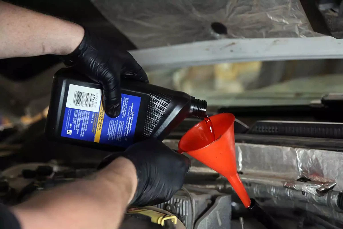 A mechanic pours fresh automatic transmission fluid into a funnel to direct the fluid into the dipstick tube.