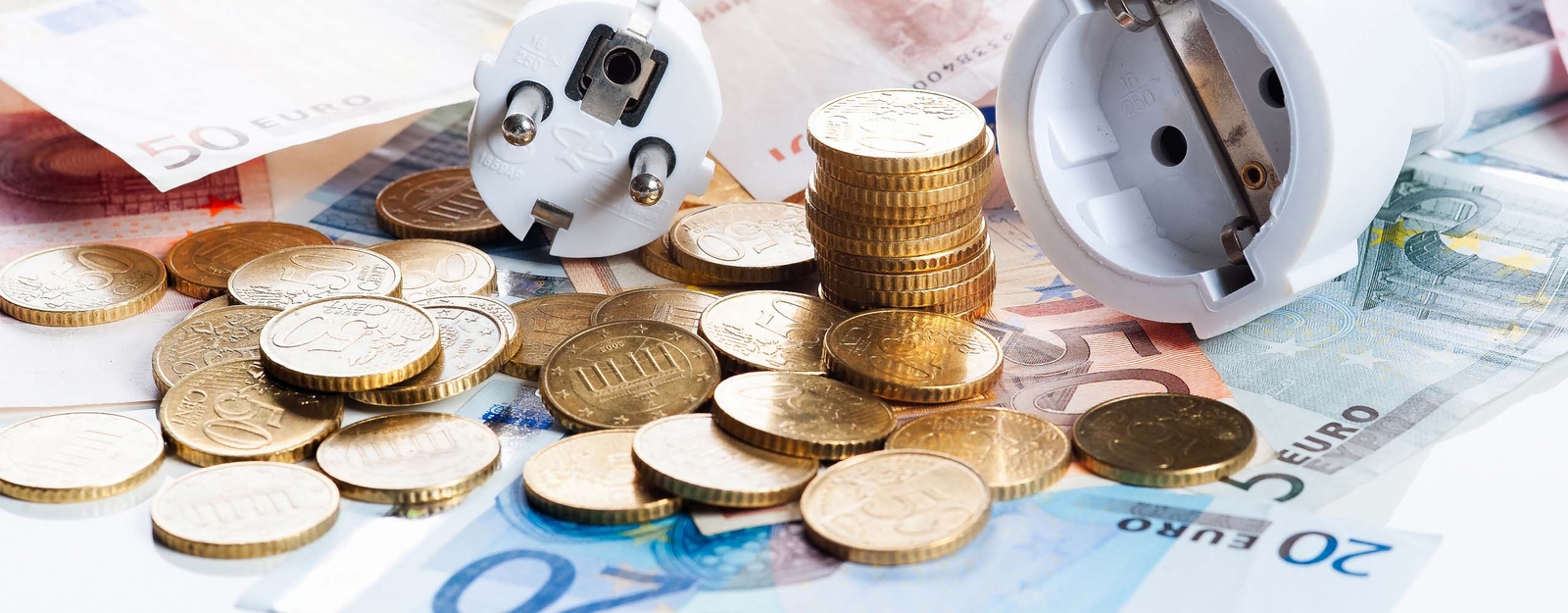 Ein abgetrennter Stecker, gestapelte und verstreute Münzen liegen auf verschiedenen Euro-Banknoten. 