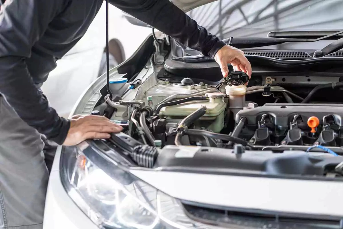 A mechanic removes the brake fluid reservoir cap. The brake fluid is darkly colored, indicating that it’s time to replace it.