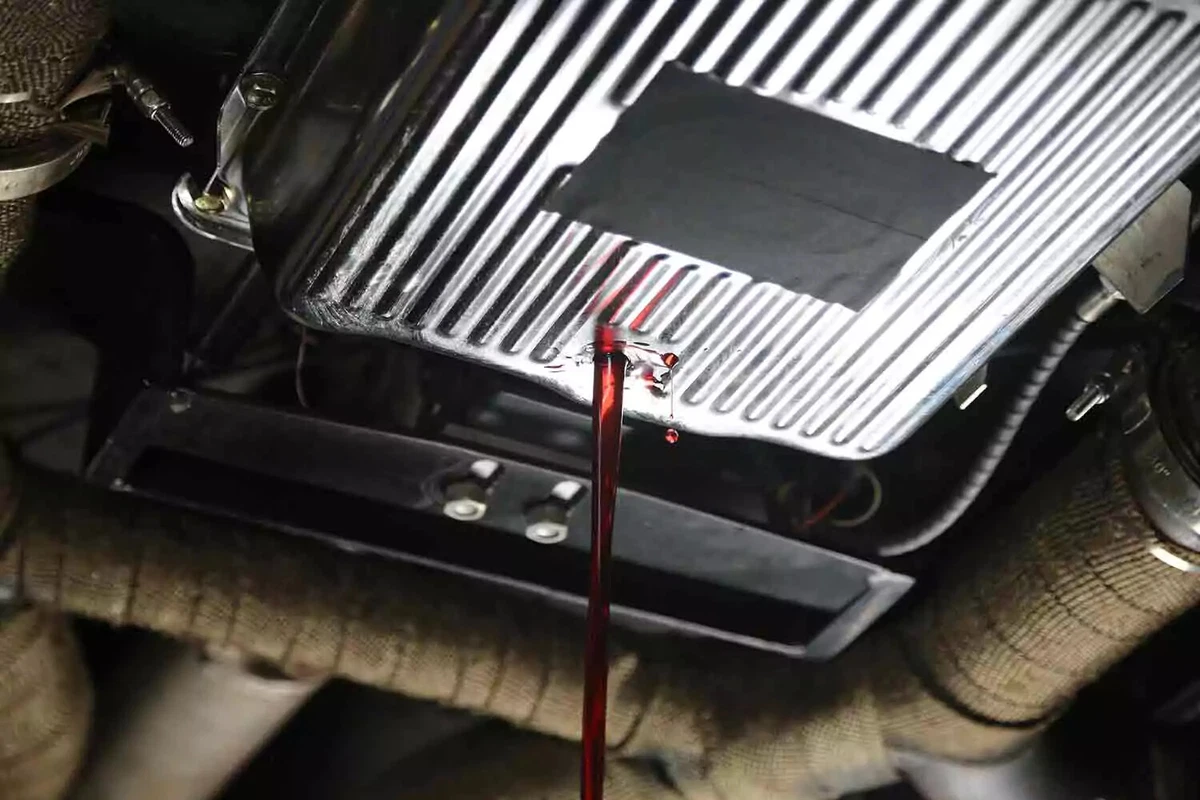 Red transmission fluid drains from a vehicle's transmission pan.