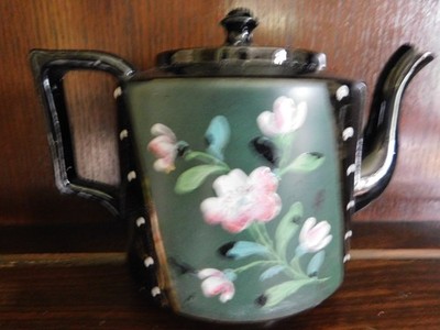 Eine alte Teekanne mit Blumenmuster handbemalt auf schwarzer Glasur
