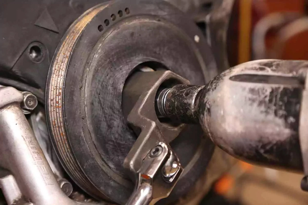 A large crank belt socket and an impact wrench are used to remove a crankshaft pulley from a Honda V-6 engine.