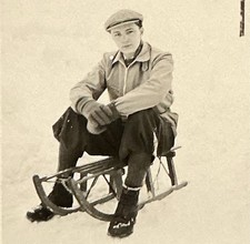 Großer Junge mit Schiebermütze sitzt nachdenklich auf einem Schlitten Rodel Foto