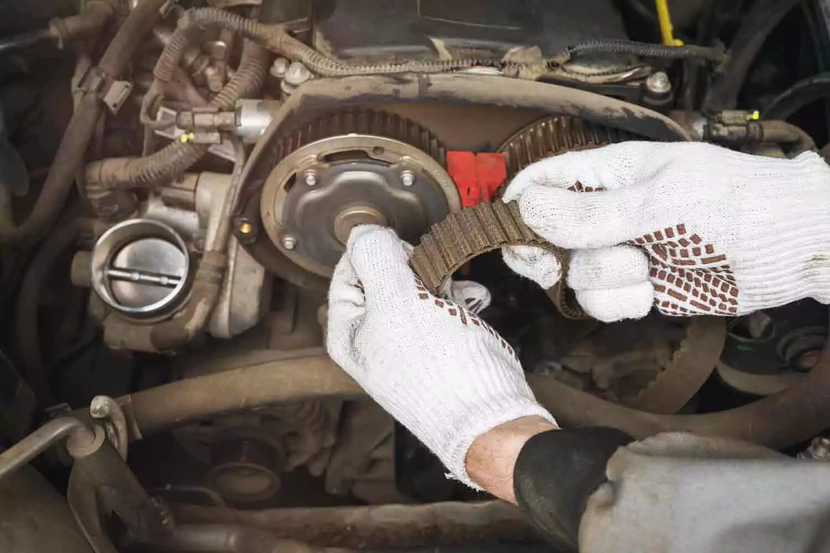 A mechanic wearing white work gloves inspects an old drive belt for wear.