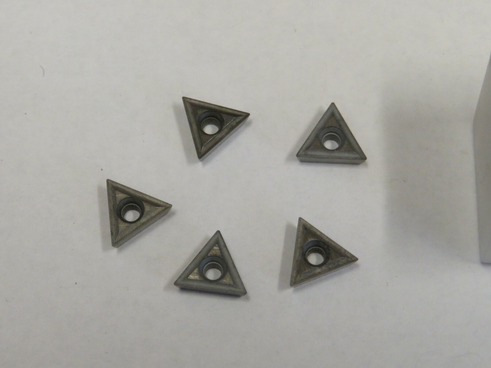 Seven gray TT-221 C2 carbide inserts with triangular black and silver cutting tips, arranged in two rows on a white surface.