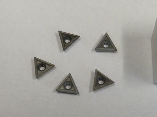 Seven gray TT-221 C2 carbide inserts with triangular black and silver cutting tips, arranged in two rows on a white surface.