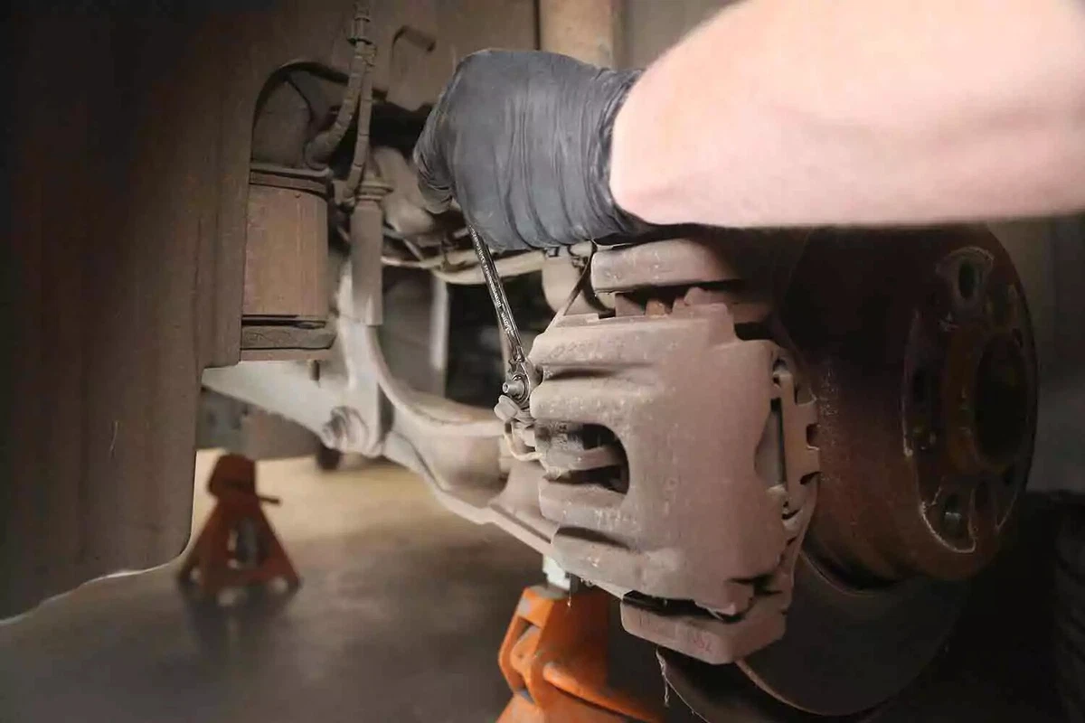 A mechanic wearing a black glove uses a socket to open a vehicle's brake bleeder.