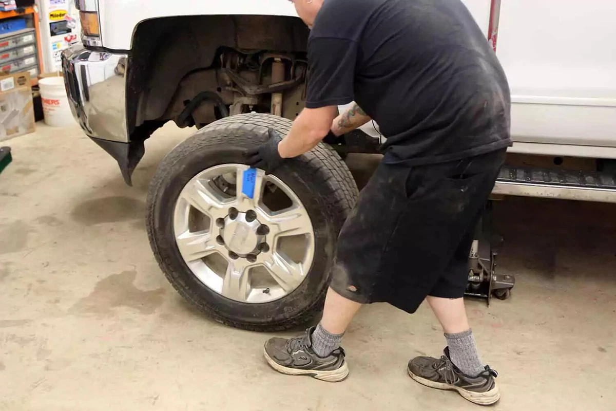 With the pickup truck supported by jack stands on all four corners, a mechanic removes the front wheel.