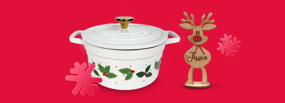 A Martha Stewart Dutch Oven Holiday Collection Holly White Enamel Cast Iron Stock Pot and a personalized wooden red-nosed reindeer ornament with the name 'Jessica' printed on the front, both lined up against a red background with snowflake stickers.