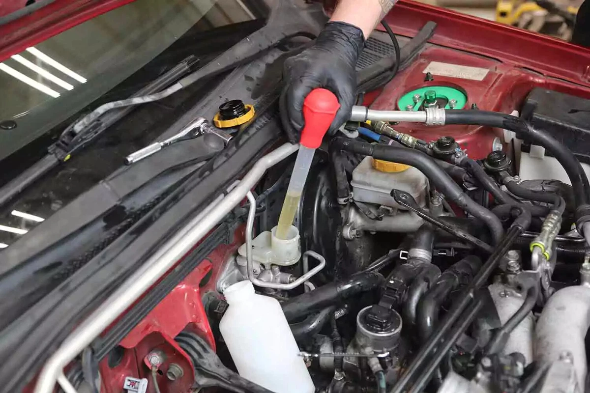 A mechanic wearing a black glove uses a squeeze-bulb extractor to remove fluid from the clutch master.