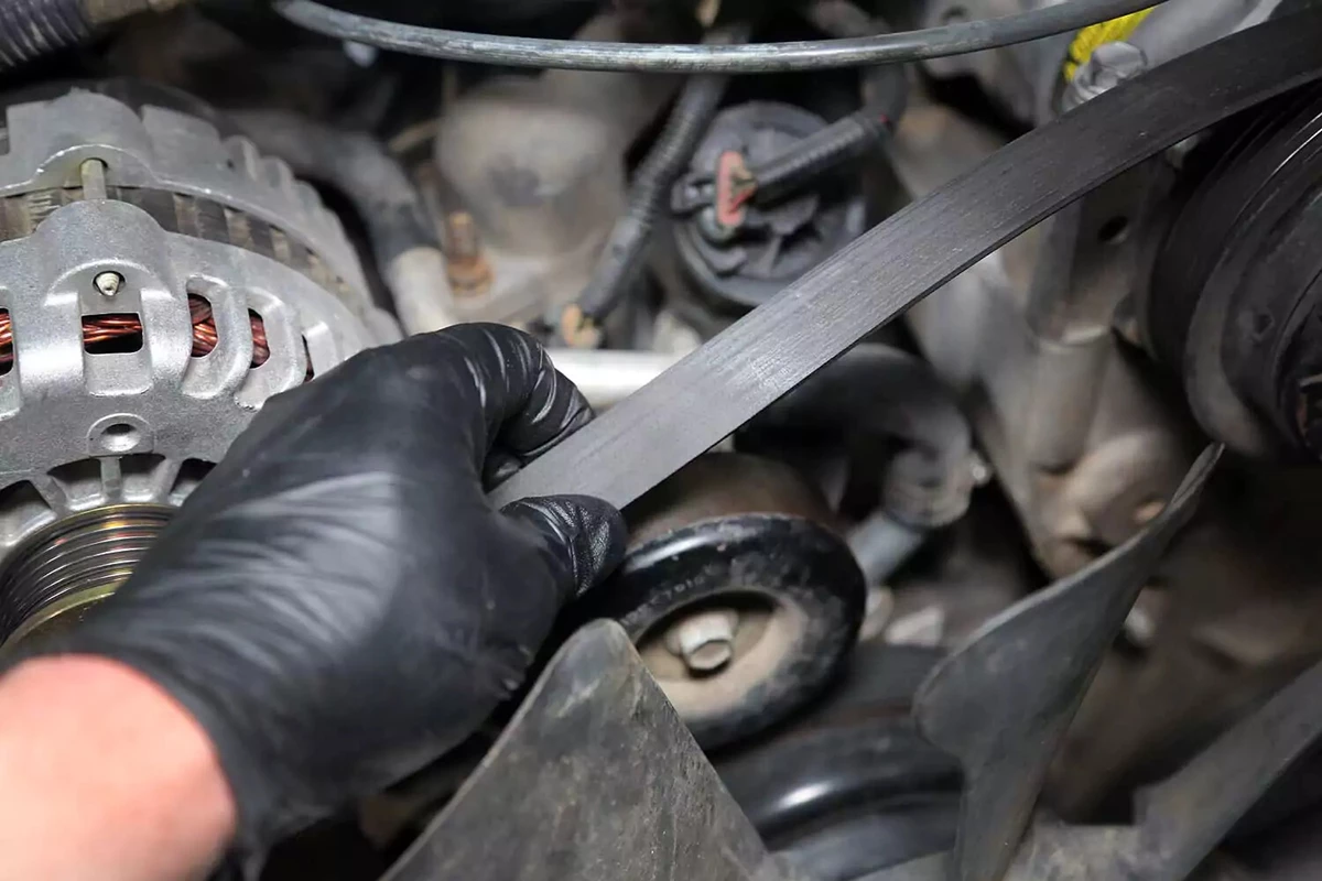 A mechanic slips the serpentine belt off the tensioner.