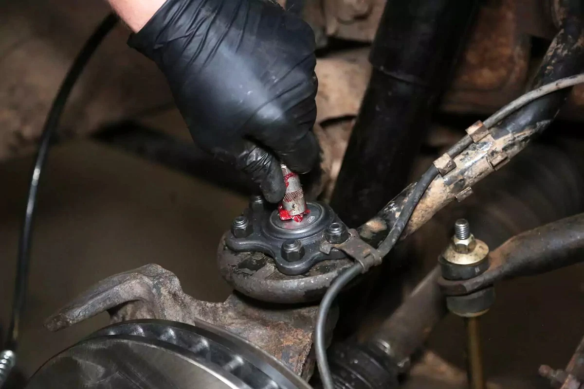 A mechanic uses a grease gun to inject grease into the new ball joint.