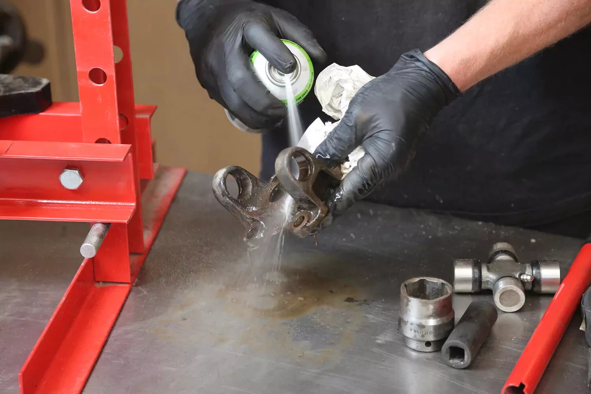 A mechanic wearing black gloves sprays a yoke with brake cleaner.