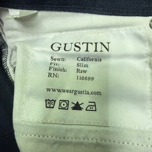 White fabric tag on Gustin jeans men 30x29 indigo raw selvedge denim slim fit made in USA with black printed text and icons.