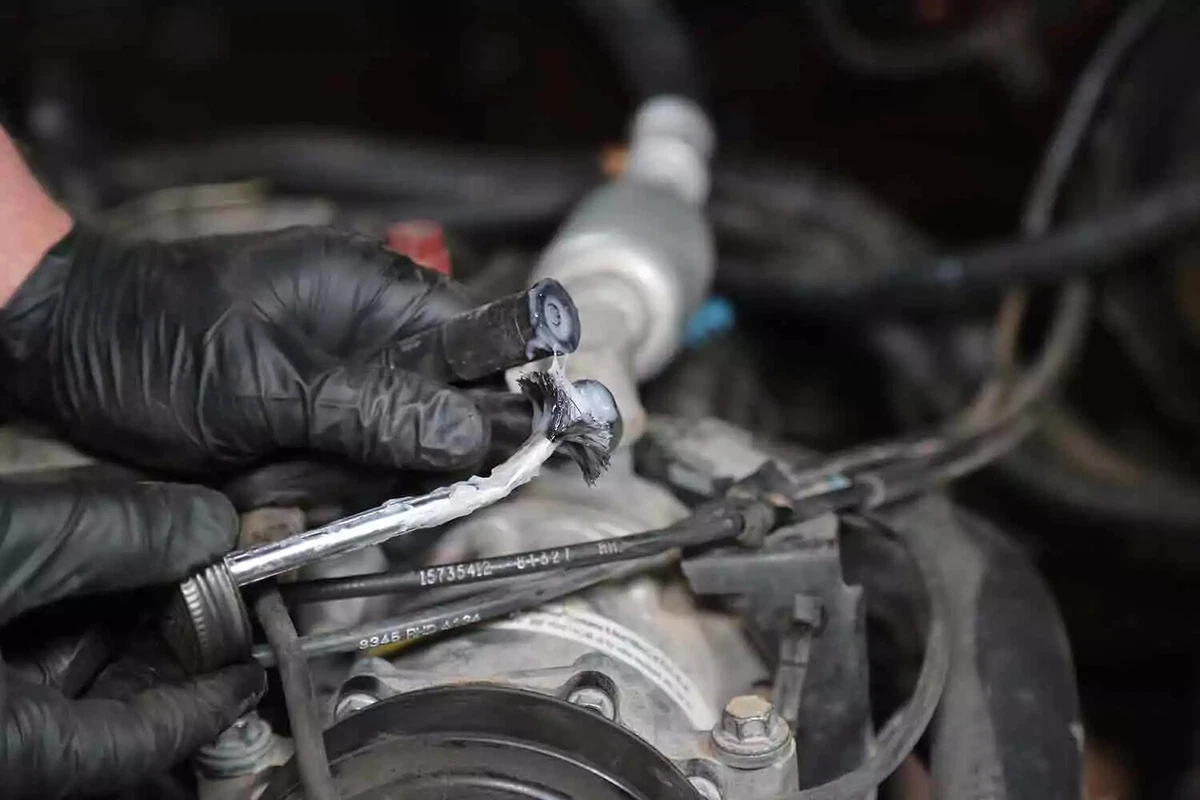 A mechanic wearing black nitrile gloves coats two spark plug wires with dielectric grease. 