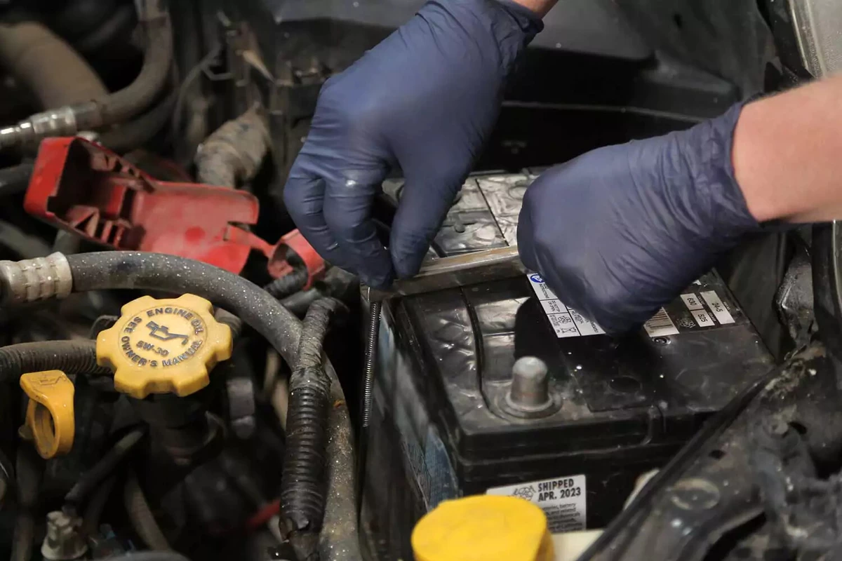 Removing a wing nut to loosen a car battery hold-down clamp.