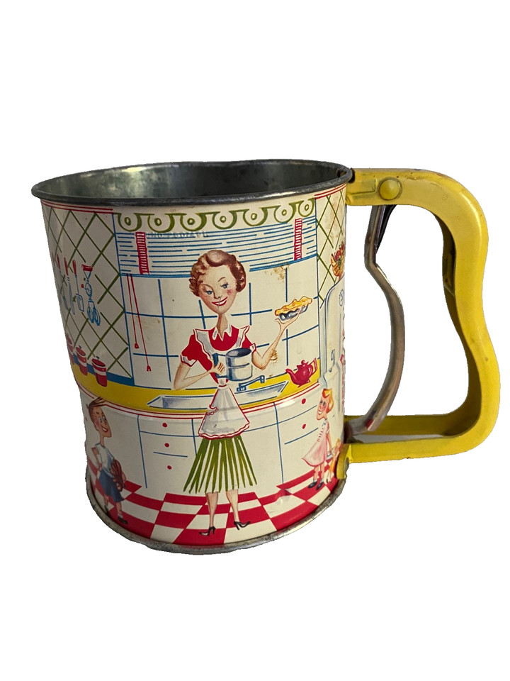 A 1950s Androck tin flour sifter illustrated with a charming kitchen scene — a working piece of mid-century folk art that doubles as vintage decor.