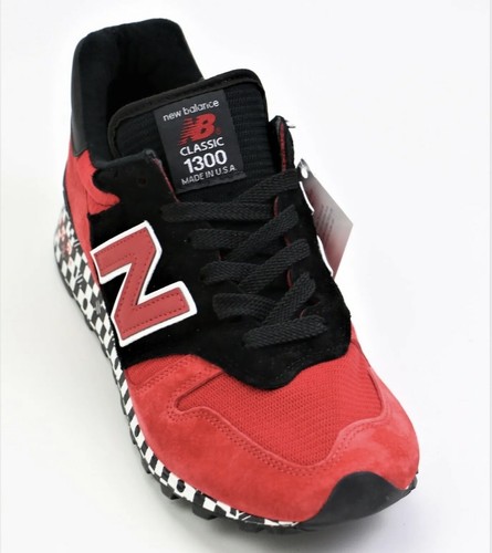 Red and black New Balance 1300 sneaker with white laces, mesh panels, and “Made in USA” label on tongue.