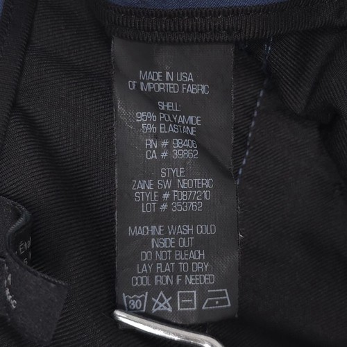 White clothing tag on black fabric with blue ZAINE SW NEOTERIC F0877210 label reading “Made in USA” and product details.