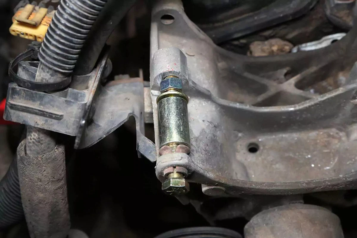 Stacking spacers and a nut onto a long bolt threaded through bushing into the alternator mounting bracket.