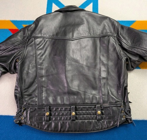 Black vintage leather Langlitz motorcycle jacket with gold studs, snap buttons, and quilted back panel on blue background.