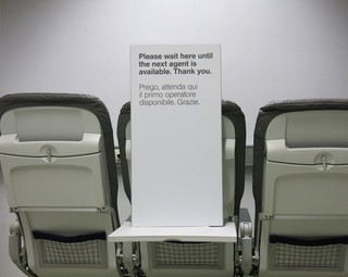 Airport information sign "Please wait here..." with Italian translation