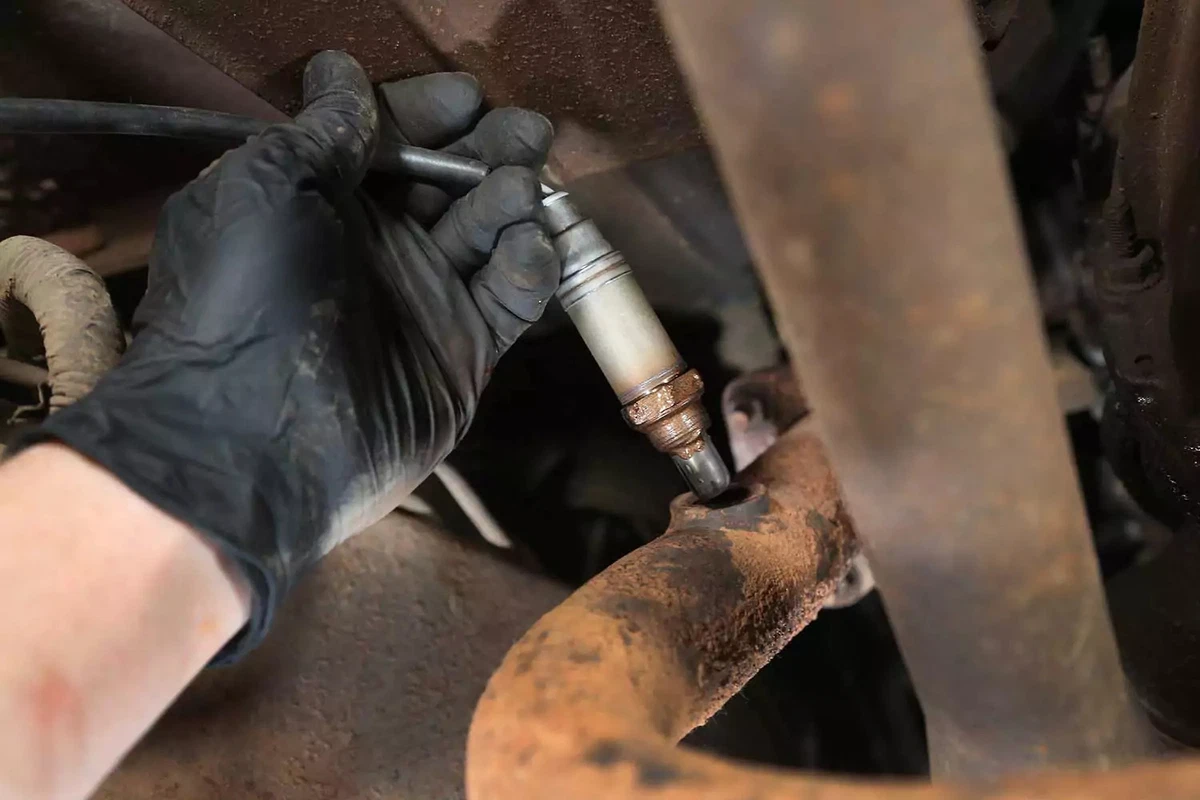 A mechanic sliding the new oxygen sensor into its exhaust bung.