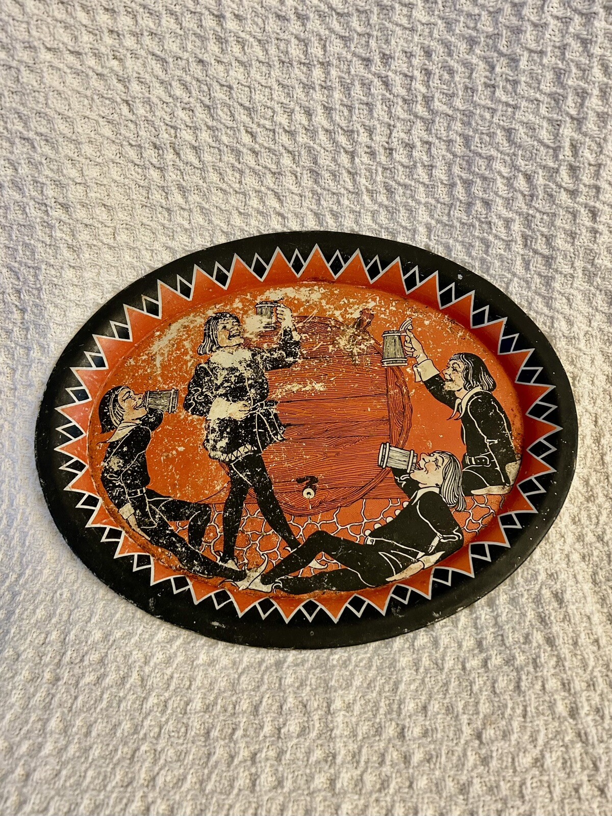 Oval tin tray printed with four cavaliers toasting and drinking around a wine barrel.