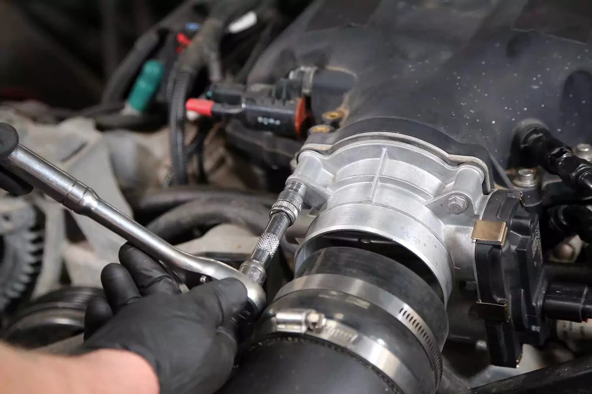 A mechanic uses a ratchet wrench to tighten the bolts connecting the new throttle body with the intake manifold.