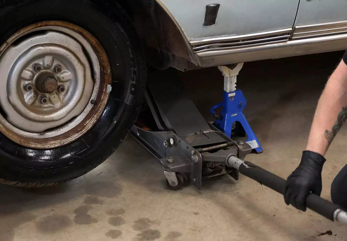 A mechanic lifting a vehicle using a floor jack and a jack stand.