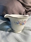 White ceramic pitcher with gold rim, pink and blue floral print, and “Made in U.S.A.” text on body.