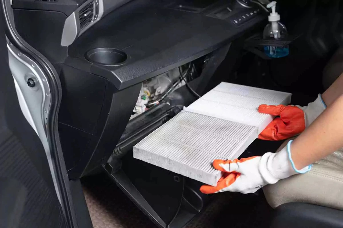 lt: A mechanic wearing orange and white work gloves compares two cabin air filters, with a used filter on the left and a new filter on the right.