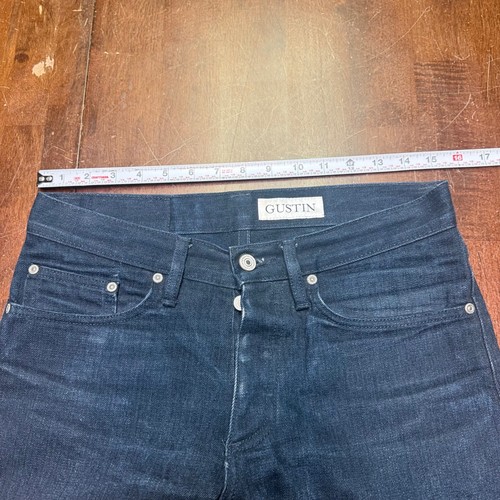 Dark blue denim slim-fit Gustin jeans with five-pocket design, button closure, and white belt loops, measured on wooden surface.
