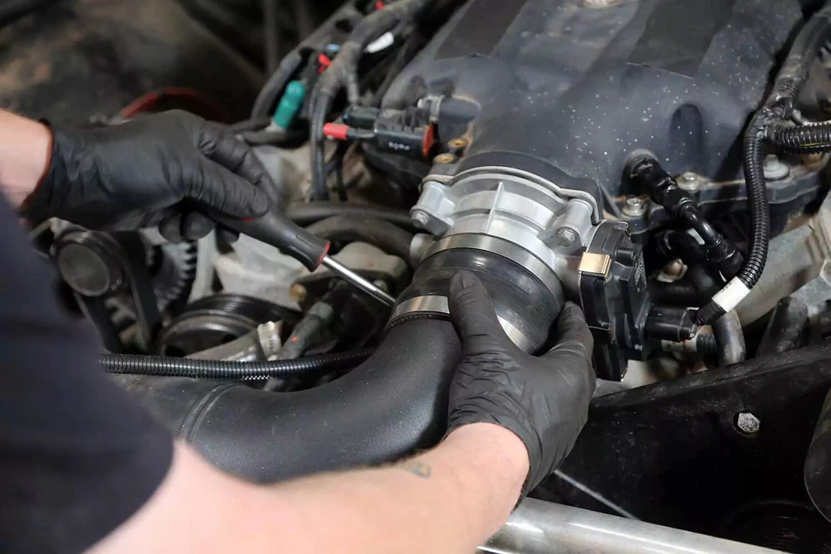 With the air intake tube reconnected, a mechanic tightens the intake tube’s hose clamp with a small socket.