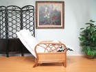 White rattan recliner chair with black trim in a light gray wall setting, next to a tall black ornamental fence.