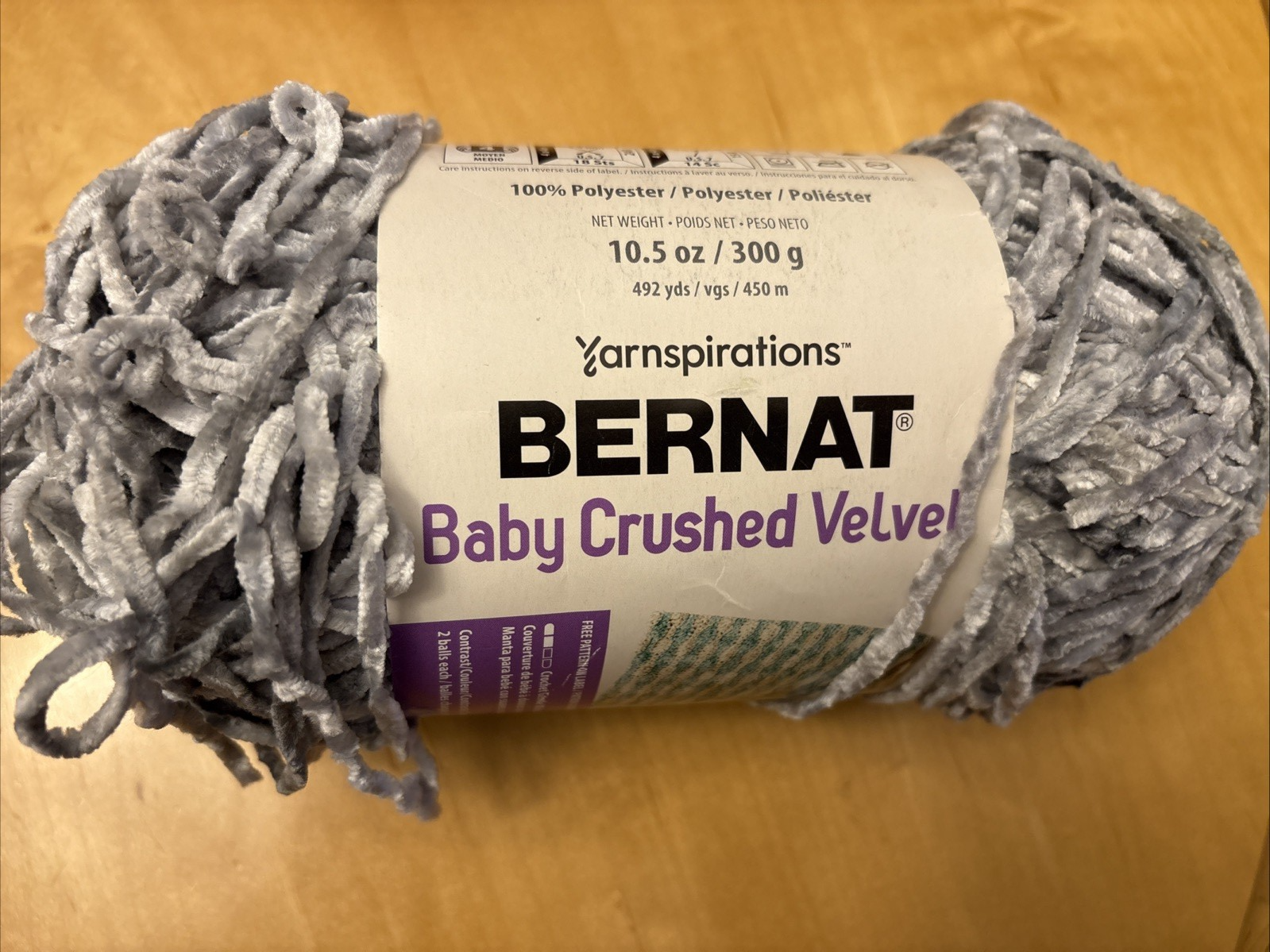 Grey mist Bernat Baby Crushed Velvet yarn ball with textured loops, wrapped in clear plastic packaging, 10.5 oz label.