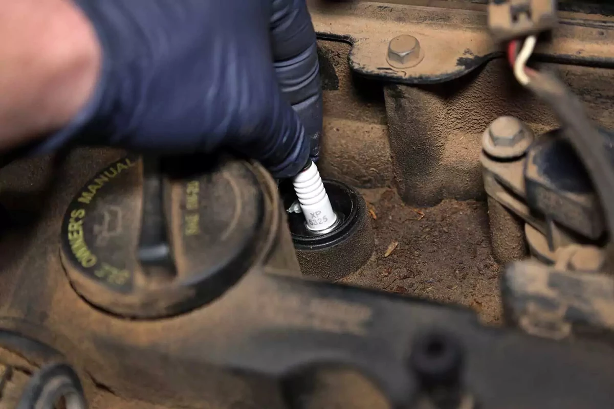 New plug being dropped into the spark plug well on an engine.