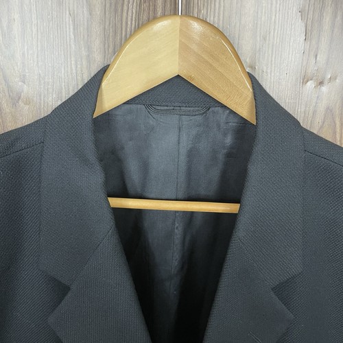 Black solid three-button blazer jacket with notch lapels, front flap pockets, and subtle textured fabric, hanging on a wooden hanger.