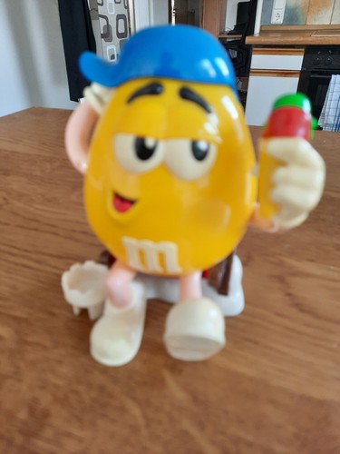 Werbefigur von M & M`s, gelbe Schokolinsenfigur mit blauer Kappe im Liegestuhl