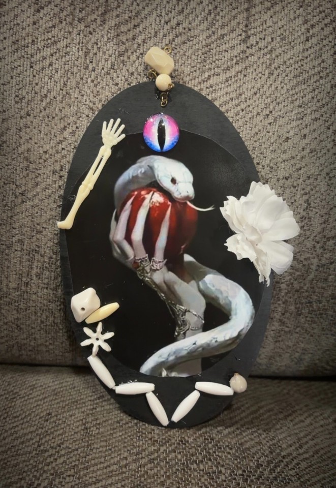 A cobra coiled around an apple rendered as a handmade wall plaque — darkly symbolic, visually striking, and totally one-of-a-kind.