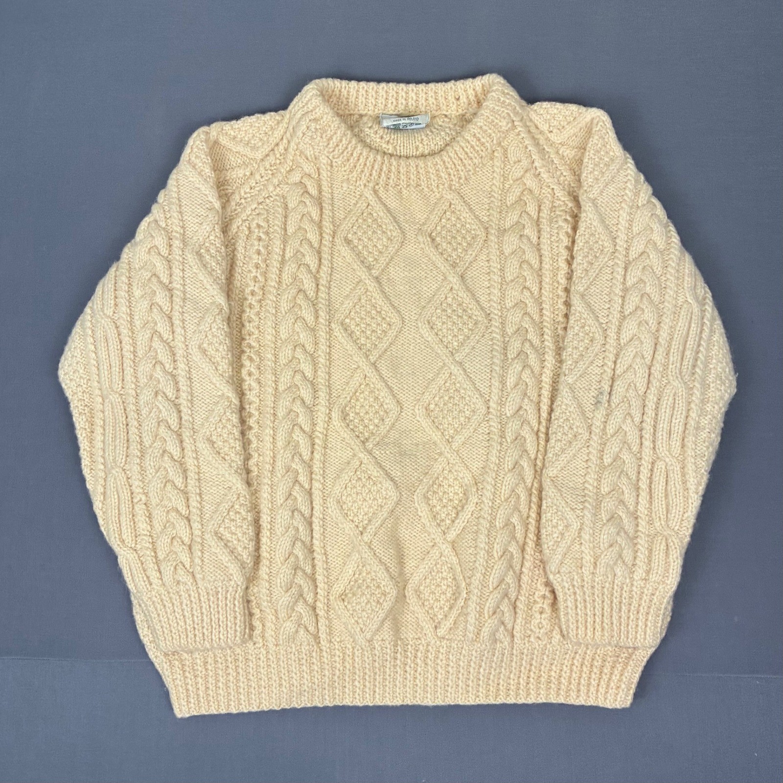 Cream hand-knit wool cable pullover sweater with mock neck, laid flat on gray background