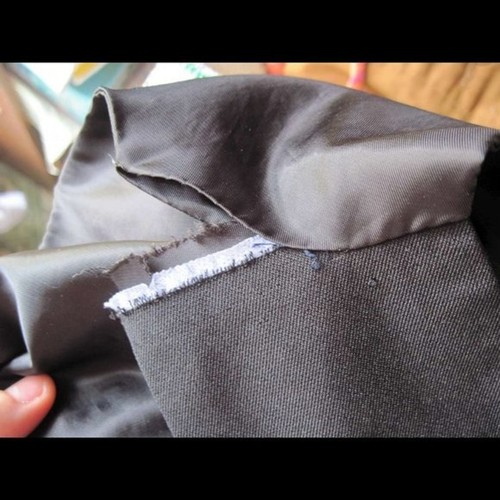 Black kids’ dress vest with frayed front edge and white patch detailing, needs mending at the seam.