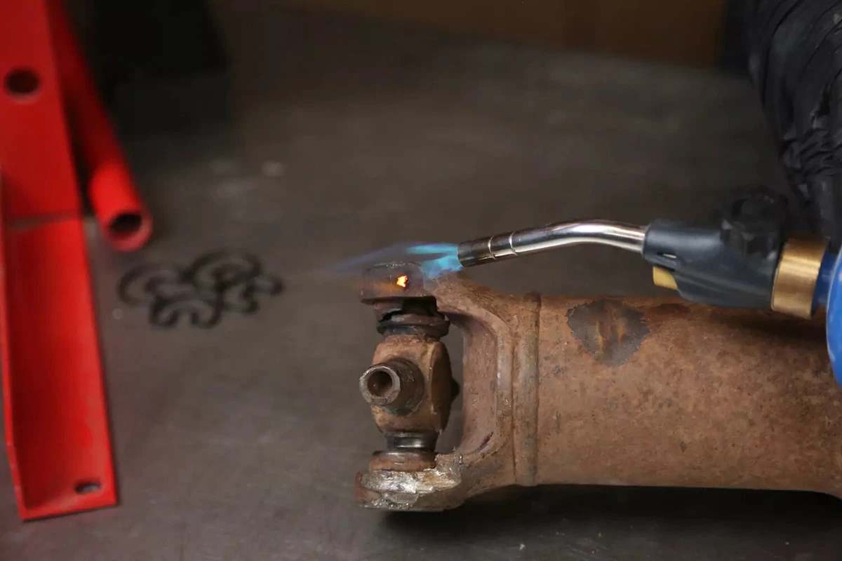 A propane torch is used to remove a thermoplastic retainer from a driveshaft.