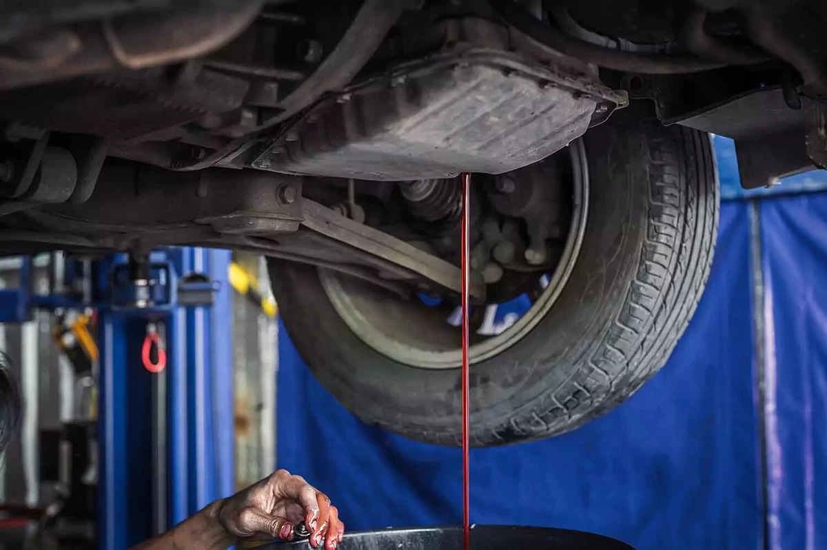 An auto mechanic drains old transmission fluid.