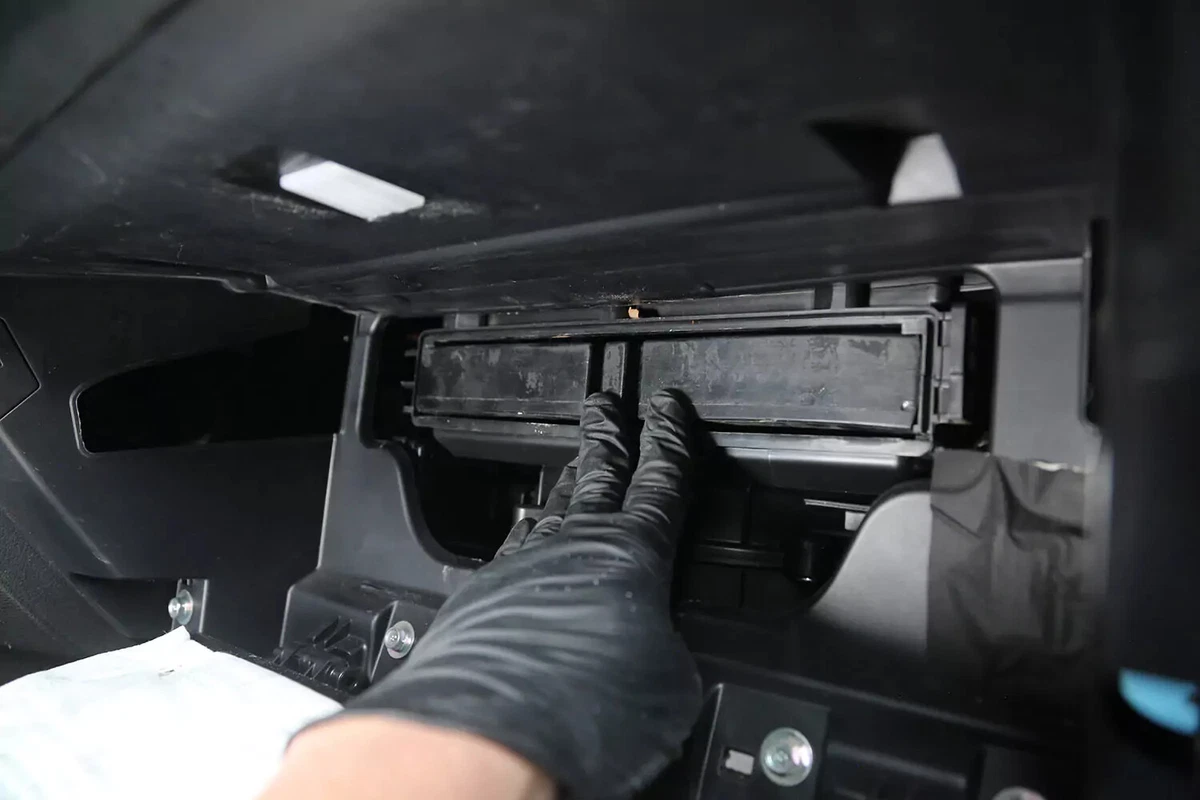 A mechanic wearing a black glove pushes the new cabin air filter into place.