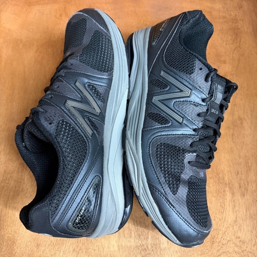 Black and gray New Balance 1540V2 men’s running shoes with silver “1540V2” text, mesh uppers, and gray laces on wooden floor.