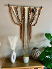 Brown, green, and cream boho macrame wall hanging with vertical stripes and fringe, displayed against a gray wall.