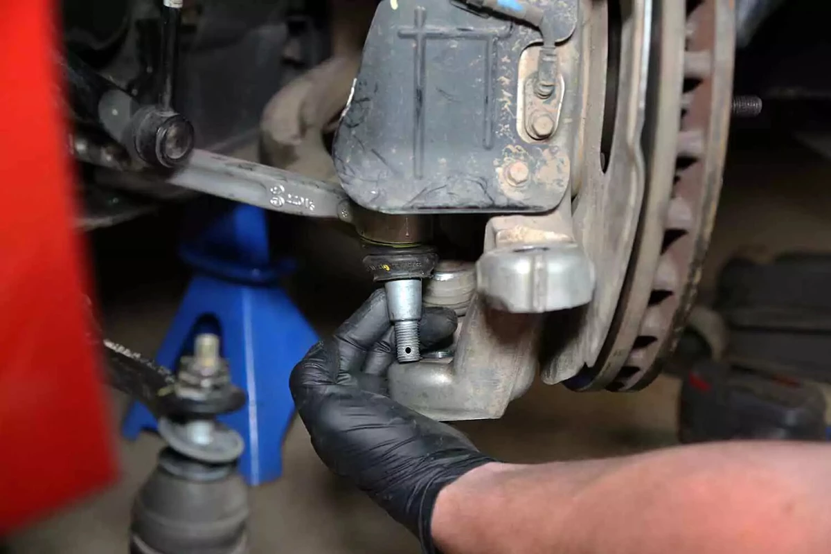 A mechanic separates a lower ball joint from the steering knuckle.